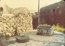 the object sitting next to the square-shaped water well looks like a stone laundry basin
				 that has been sitting there unused for a long time